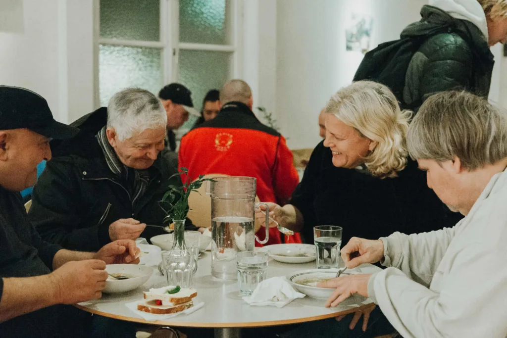 Personer på Soppmässan sitter runt ett bord och äter